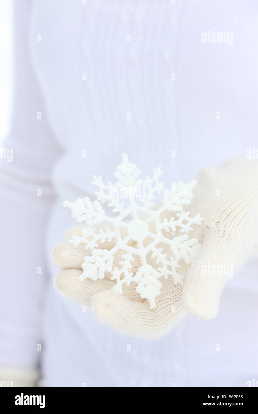 Le mani con guanti invernali tenendo premuto il simbolo del fiocco di neve a forma di albero di Natale ornamento Foto Stock