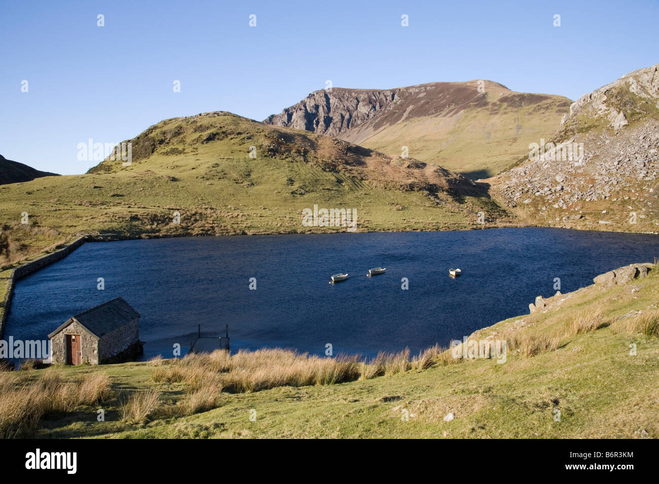 Rhyd DDU Gwynedd Galles del Nord dicembre guardando attraverso Llyn y dywarchen con una casetta per barche e tre barche da pesca ormeggiate nel Parco Nazionale di Eryri Snowdonia Foto Stock
