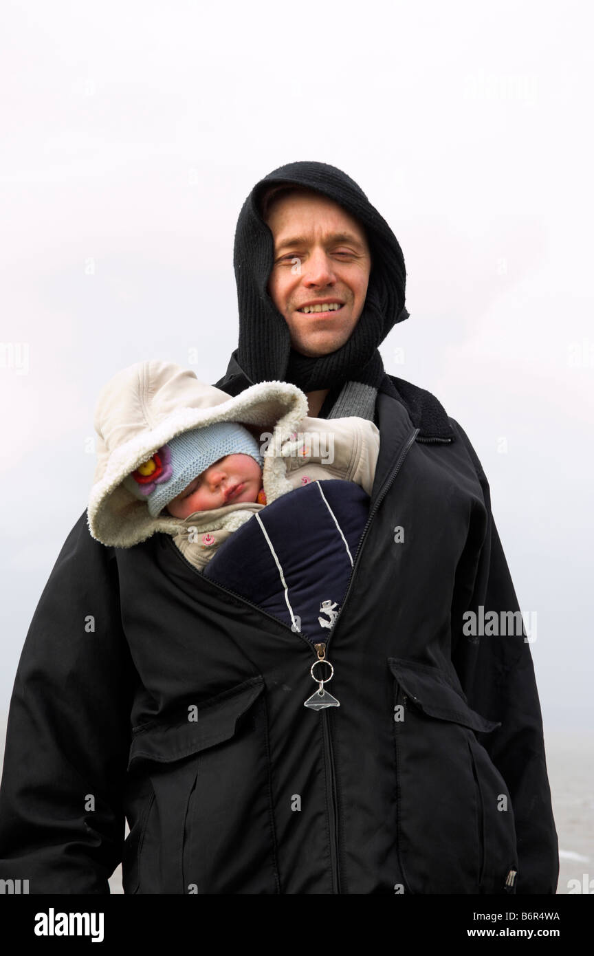 Padre che trasportano figlia infante sotto il cappotto invernale a freddo Foto Stock
