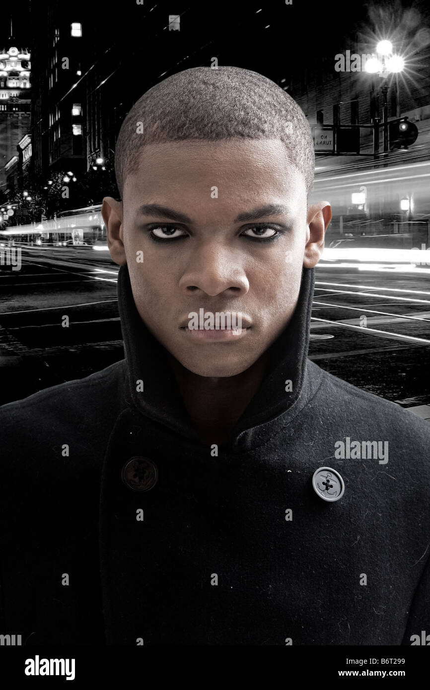 L'uomo africano con smokey eyes e mantello nero di notte su una strada con le auto in movimento in bianco e nero Foto Stock