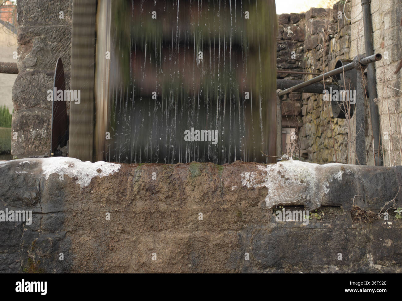 Un lavoro ruota di acqua su un freddo inverno mattina nel Derbyshire con il gocciolamento di acqua spray di congelamento sul muro di pietra Foto Stock