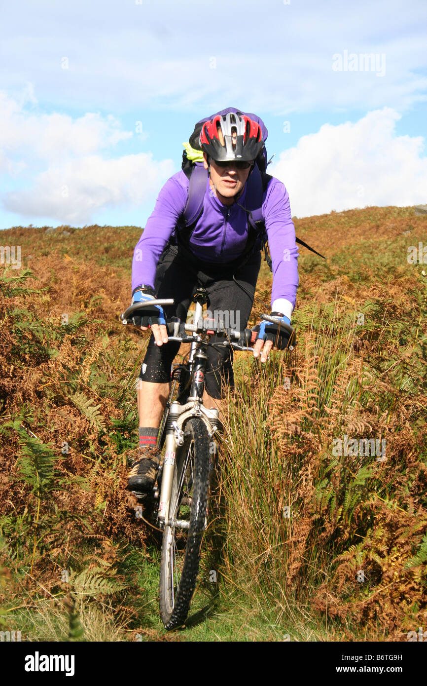 Maschio adulto mountain biker la discesa attraverso bracken su off-road ride in North York Moors Foto Stock