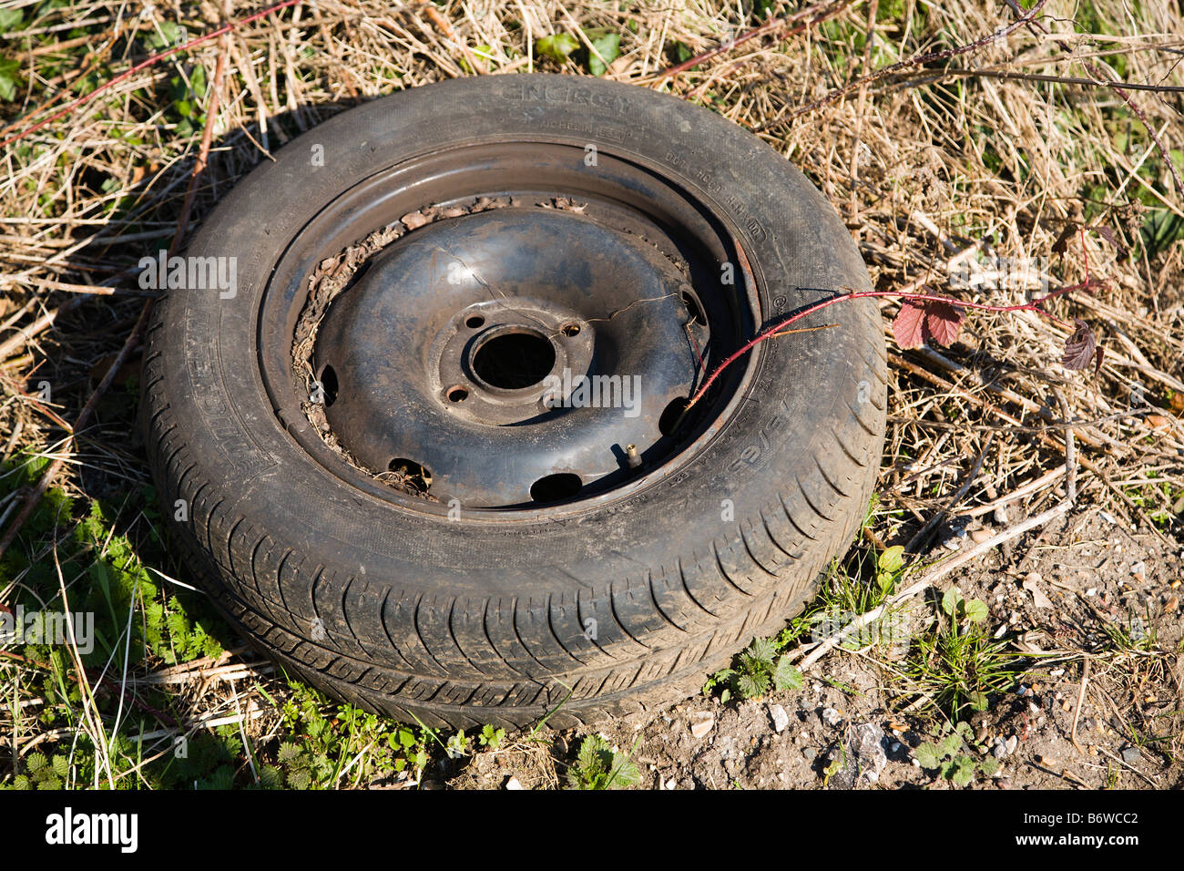 Una vecchia auto abbandonate la ruota e il pneumatico oggetto di dumping dal lato della strada. Foto Stock