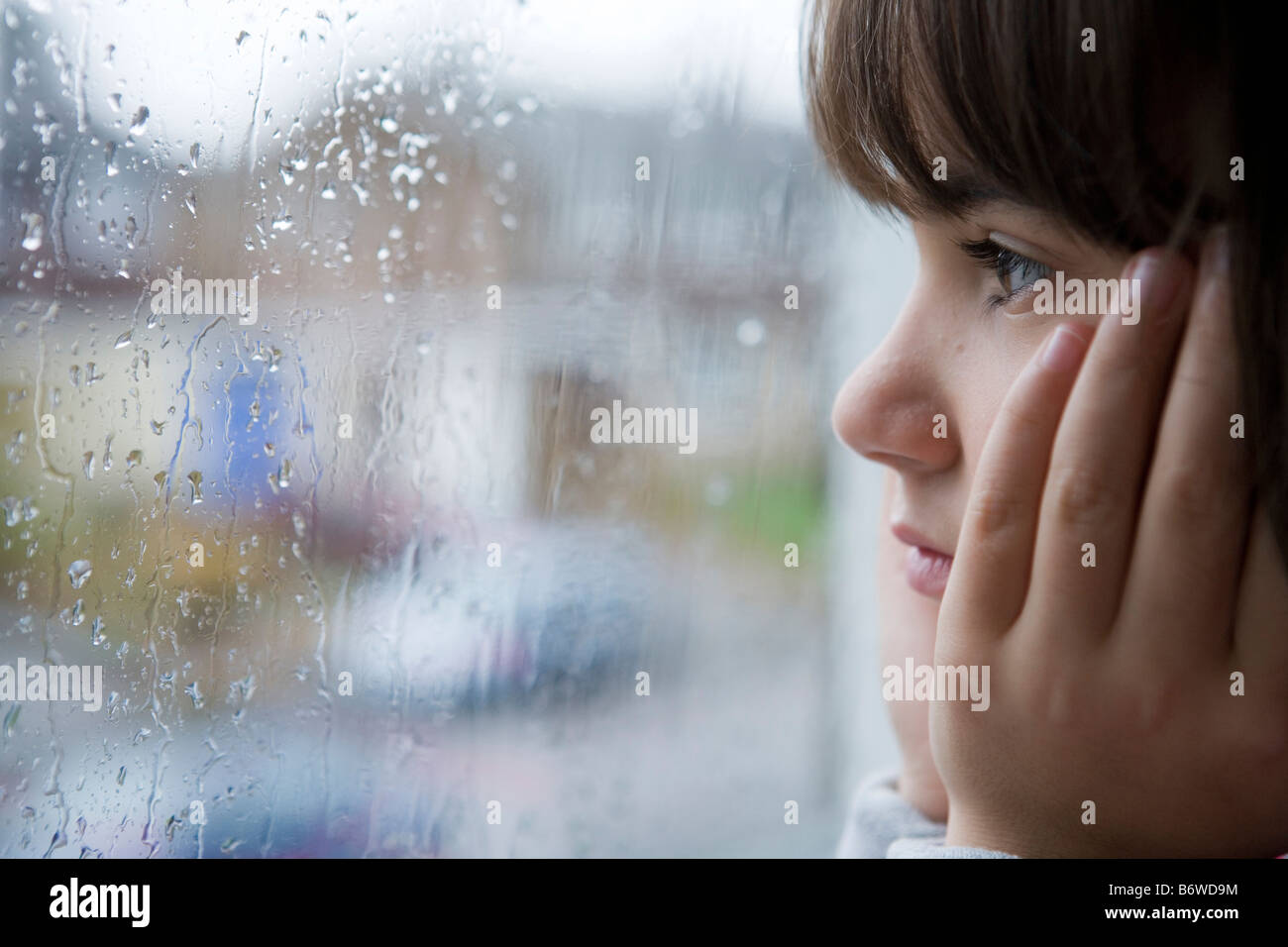 Un giovane bambino guardando fuori della finestra sul giorno di pioggia Foto Stock