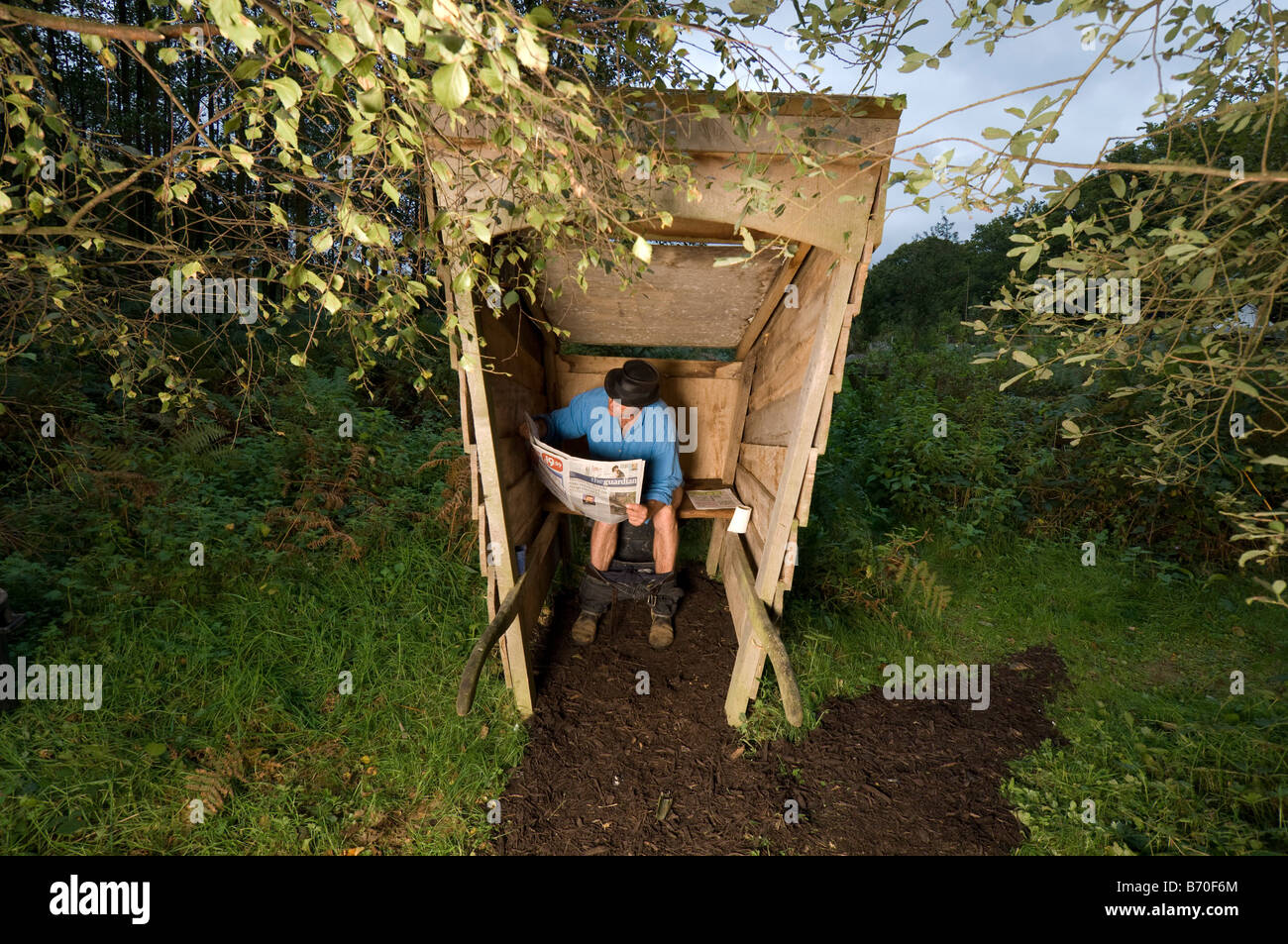 Off Grid lifestyle. L'uomo la lettura del tutore in una toilette esterna Foto Stock