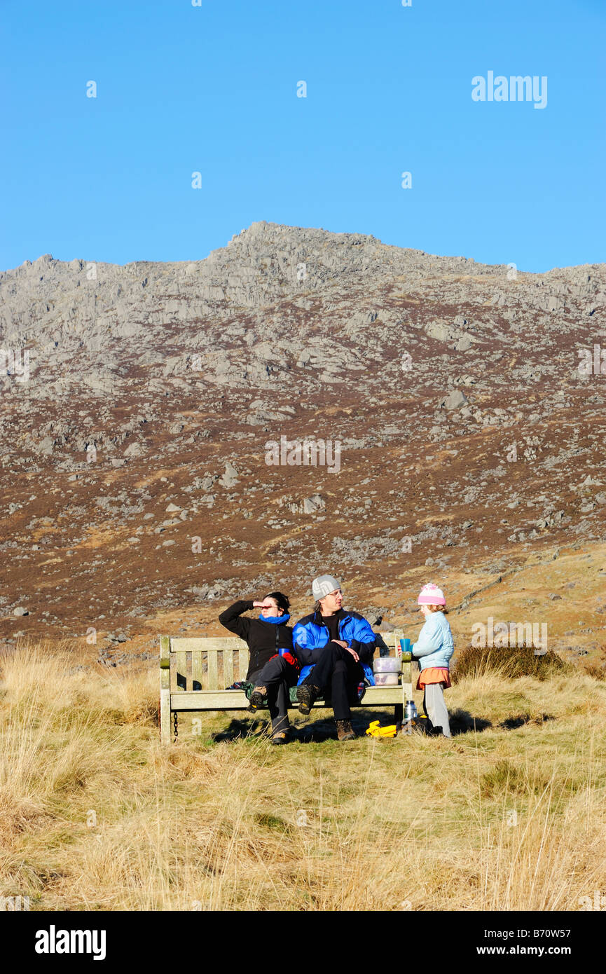 Famiglia in appoggio su una panca in Snowdonia, il Galles del Nord, in inverno al sole con Glyder Fawr in background. Foto Stock