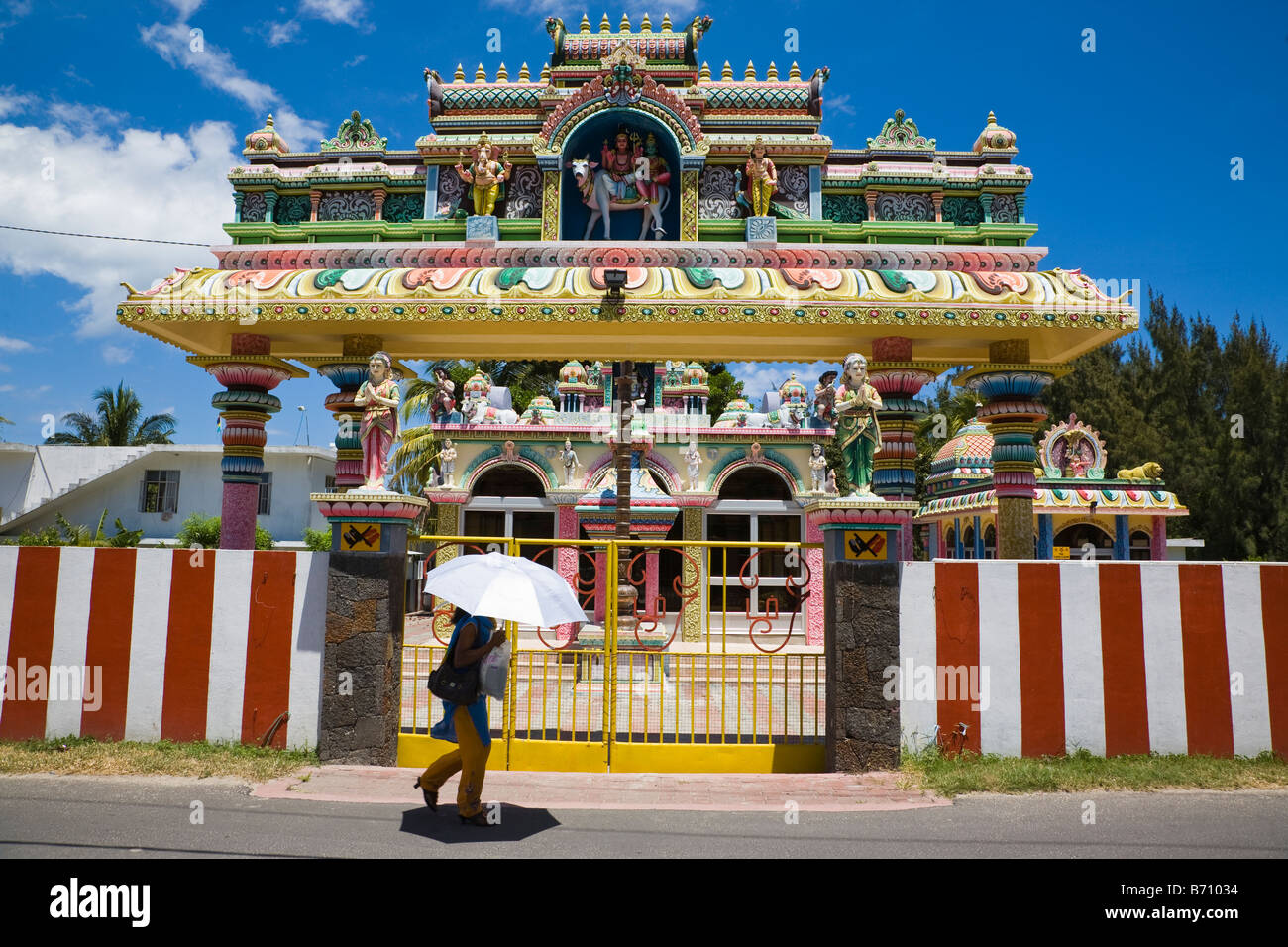 Esterno del tempio indù nei pressi del Grande Baie in Mauritius con una donna che cammina riparando sotto un ombrello da una forte luce solare Foto Stock