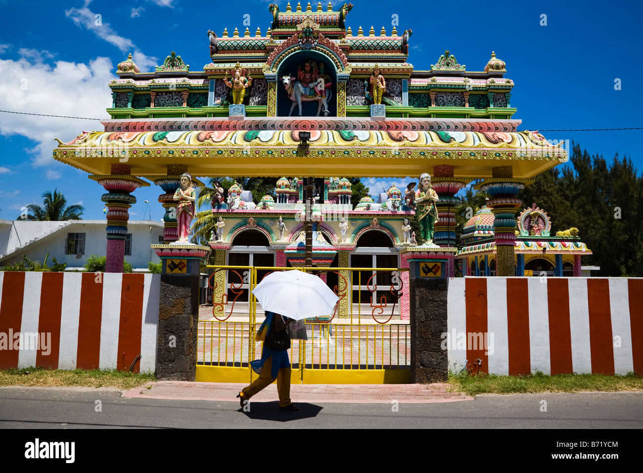 Esterno del tempio indù nei pressi del Grande Baie in Mauritius con una donna che cammina riparando sotto un ombrello da una forte luce solare Foto Stock