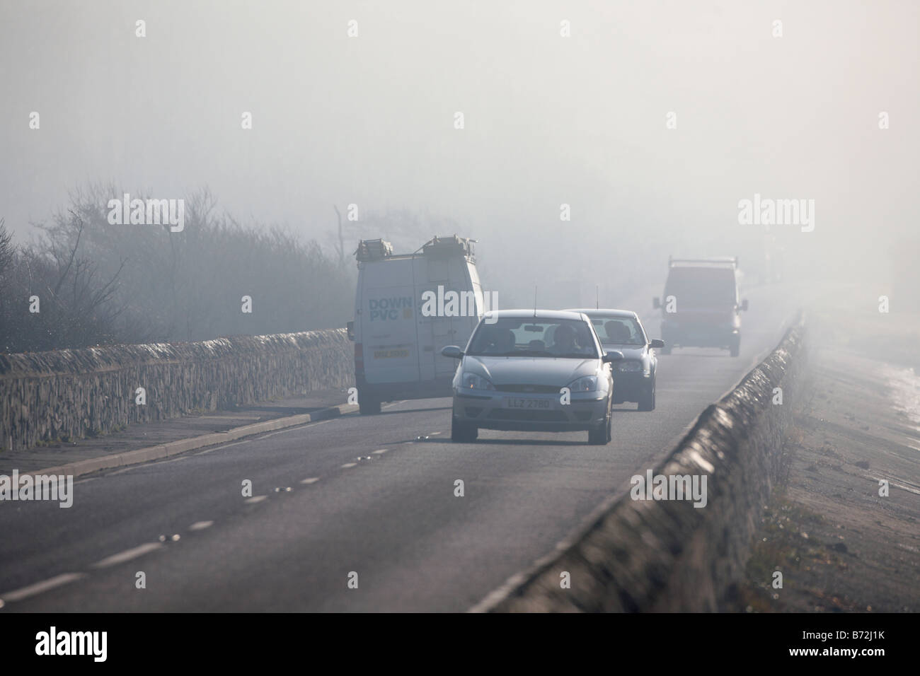 Auto e furgoni guidando lungo una nebbia strada costiera di mattina nella contea di Down Irlanda del Nord Regno Unito Foto Stock