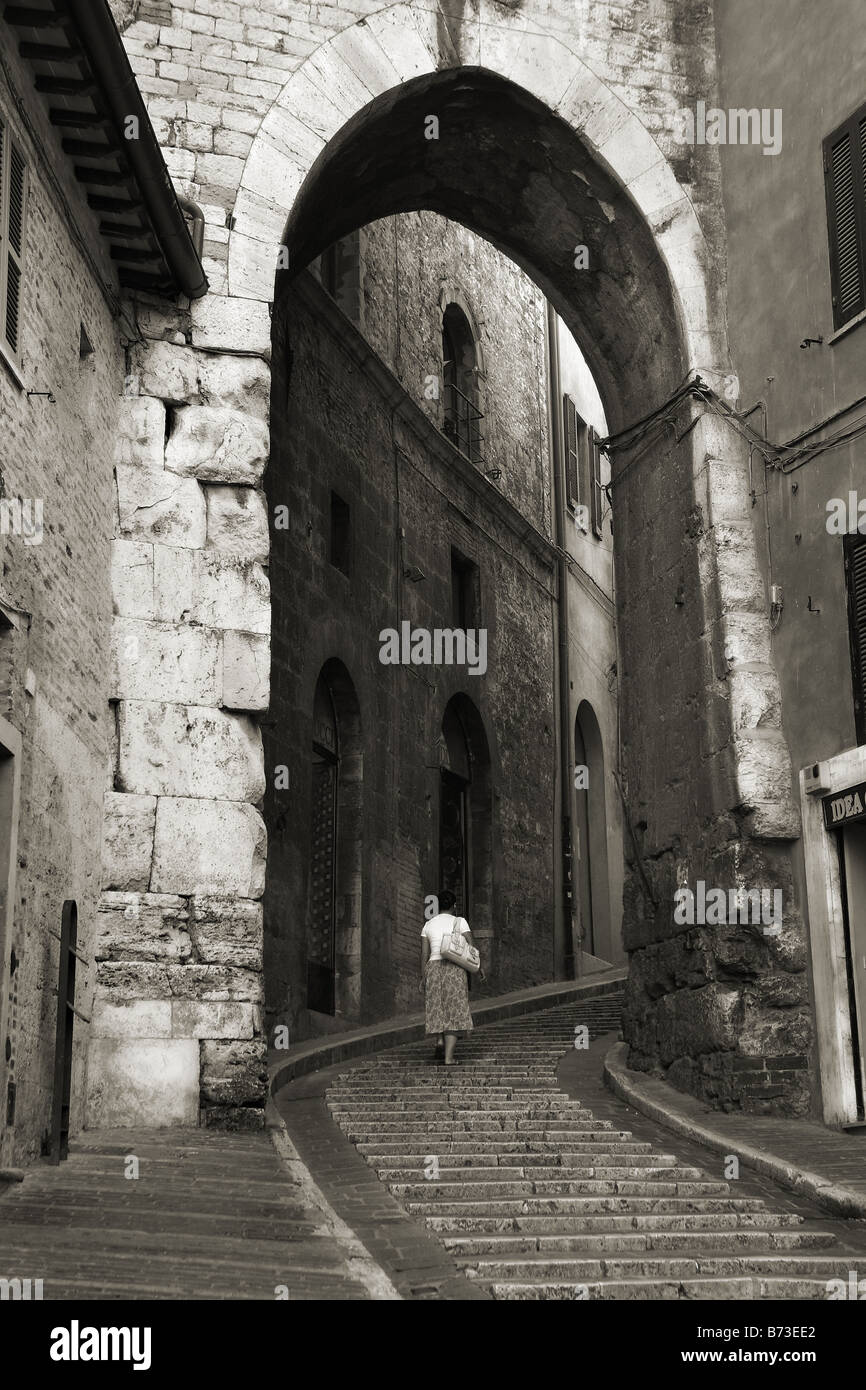 Una donna salire a piedi a gradini in pietra attraverso un arco in Perugia, Italia Foto Stock