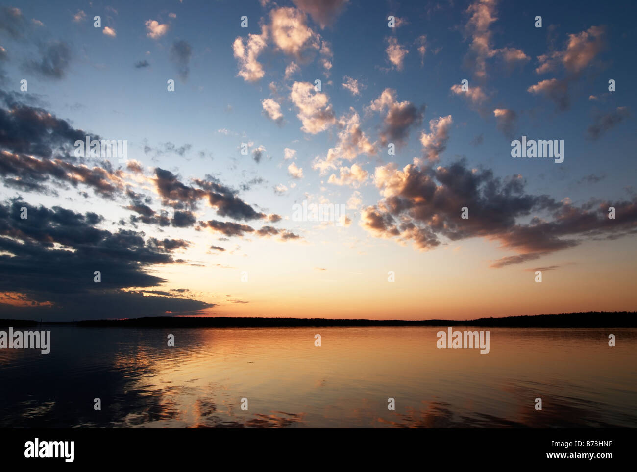 Bel tramonto dal lago calmo con soffici nuvole contro inscurimento cielo blu, Asikkala, Finlandia Foto Stock