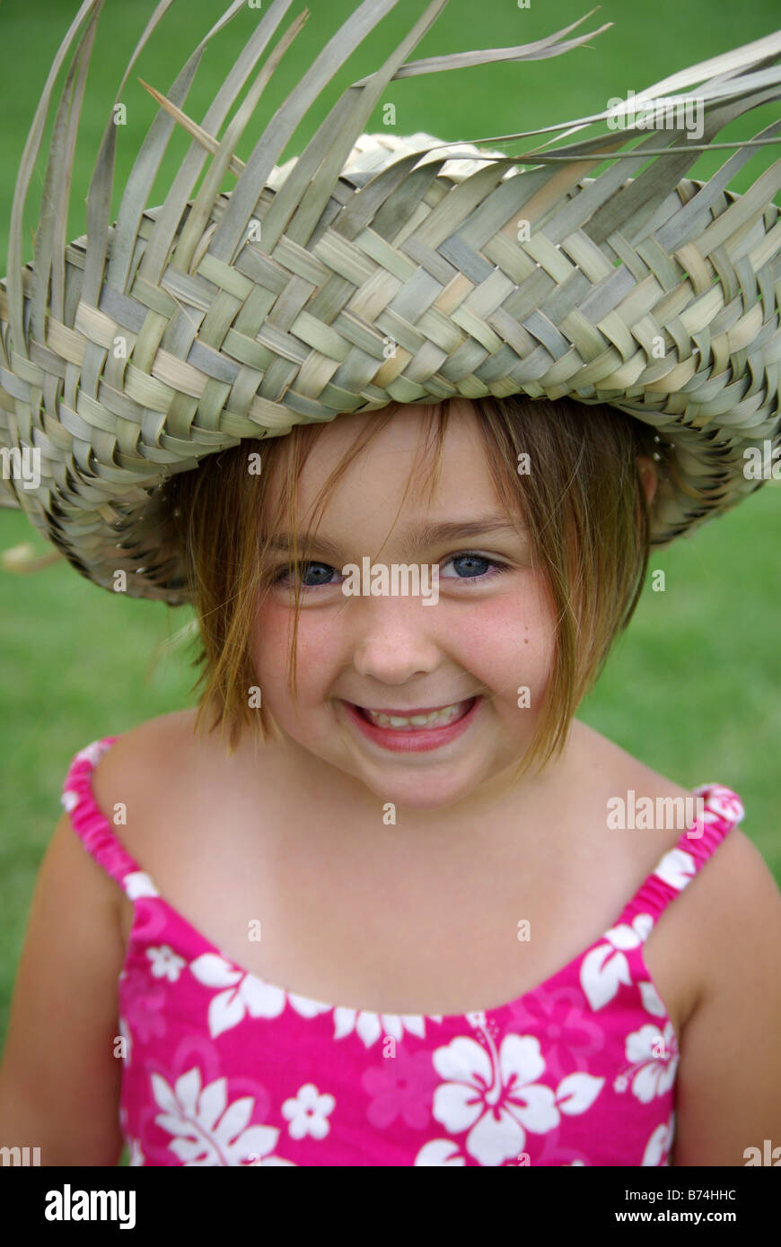 Un sorridente 5 anno vecchia ragazza che indossa un cappello di paglia e vestito tropicale guarda nella telecamera. Foto Stock