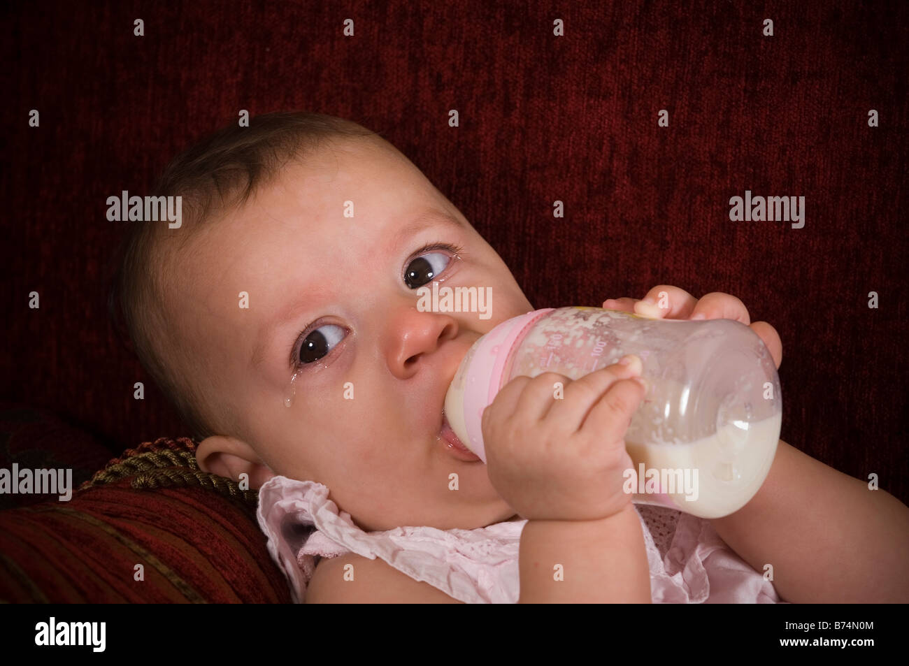 Ragazza infantile di bere latte dalla bottiglia durante il pianto Foto Stock