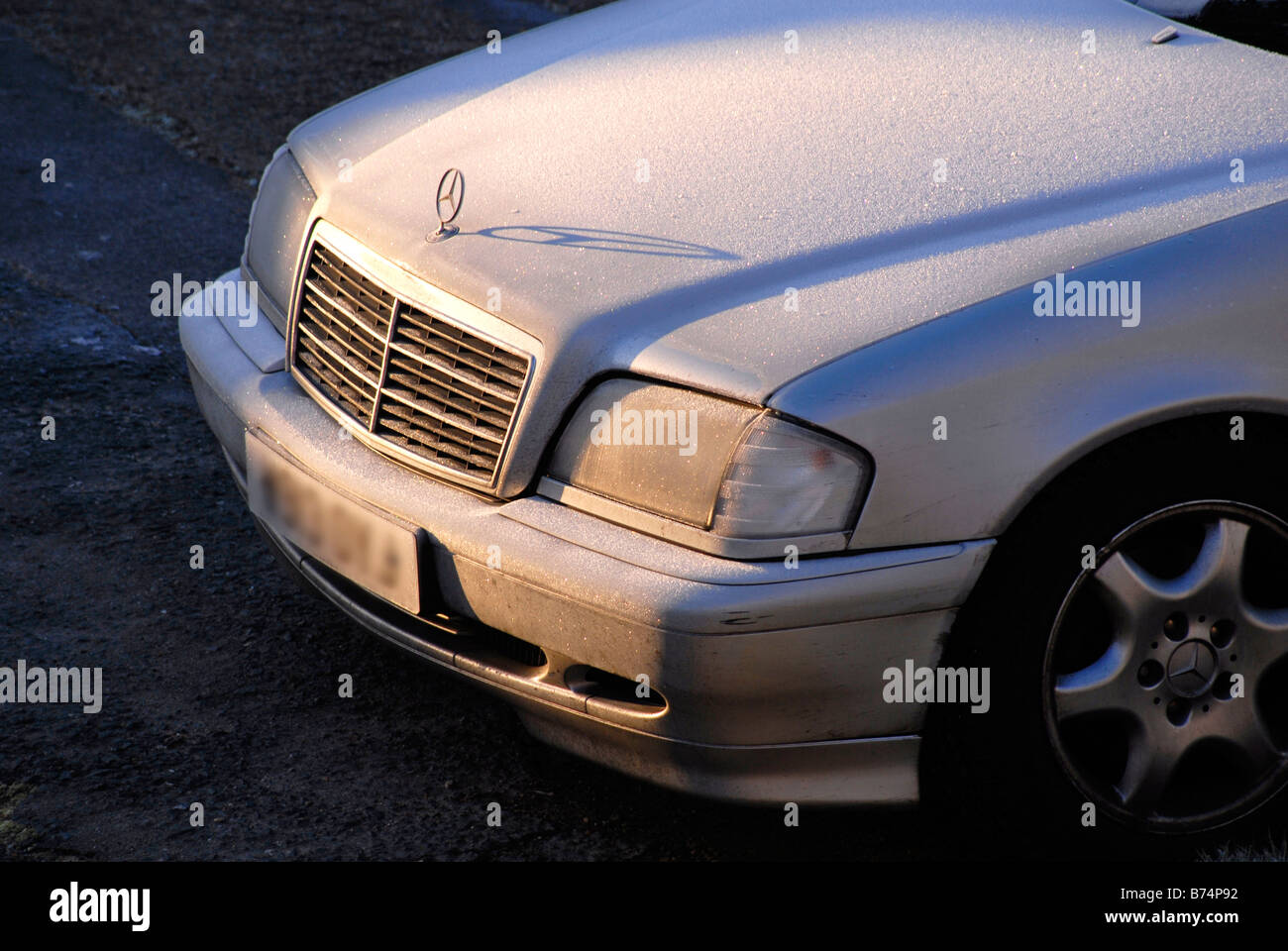 Sole che splende su ghiaccio sul cofano di argento auto Mercedes, con ombra di Mercedes logo sul cofano Foto Stock