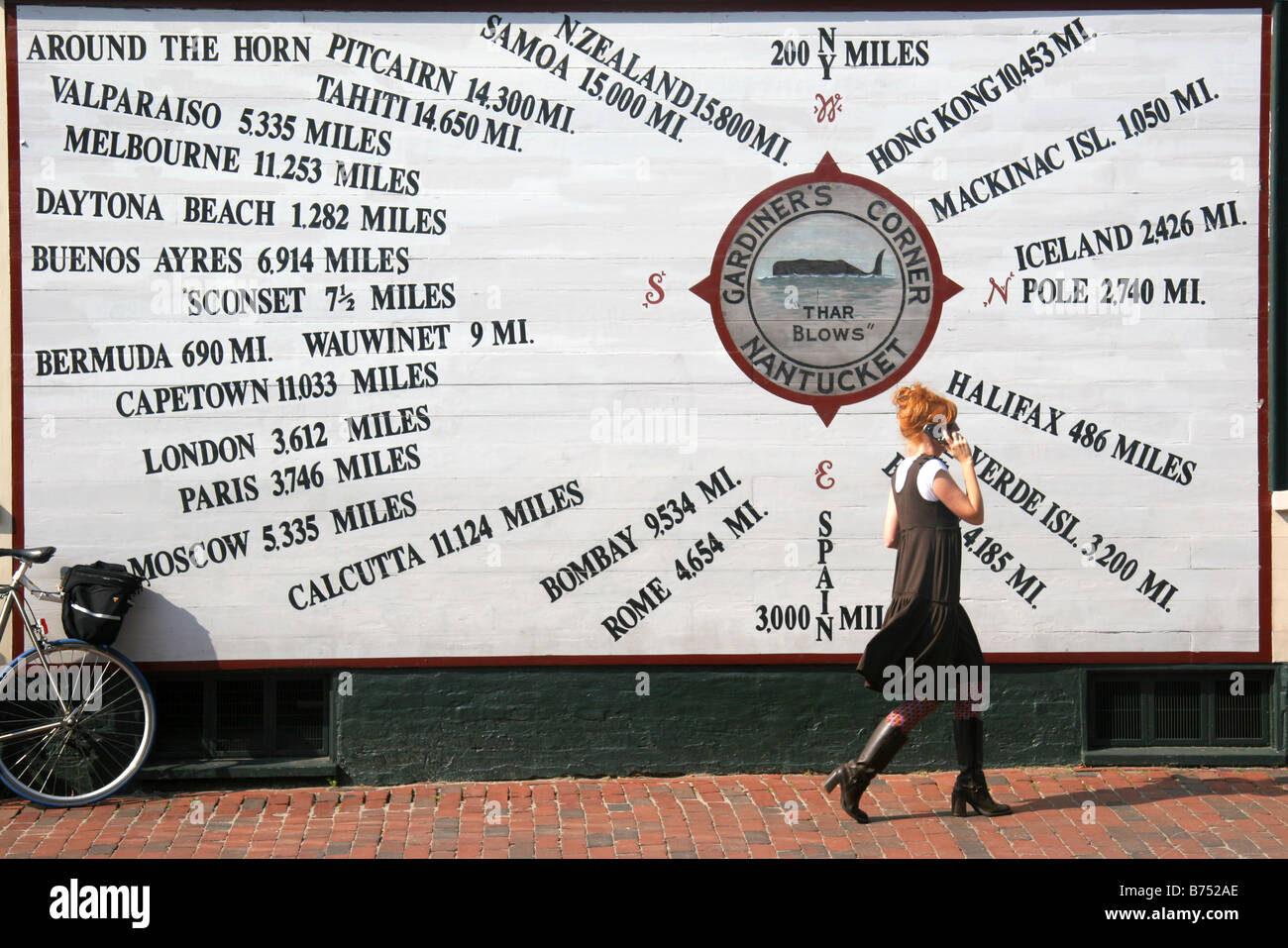 Donna passato a piedi Distanza dal mondo segno della città mentre parli al telefono cellulare in Nantucket Cape Cod STATI UNITI D'AMERICA Foto Stock