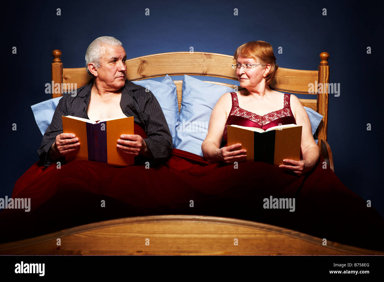 Coppia senior nel letto di interrompere la loro lettura per qualcosa di più interessante Foto Stock