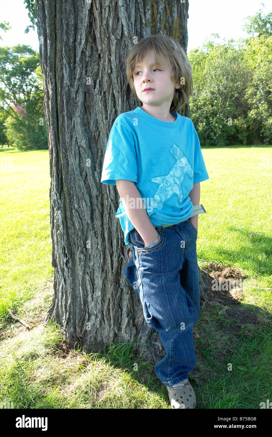 6 anno vecchio ragazzo con le mani nelle tasche al fianco di albero, Winnipeg, Canada Foto Stock