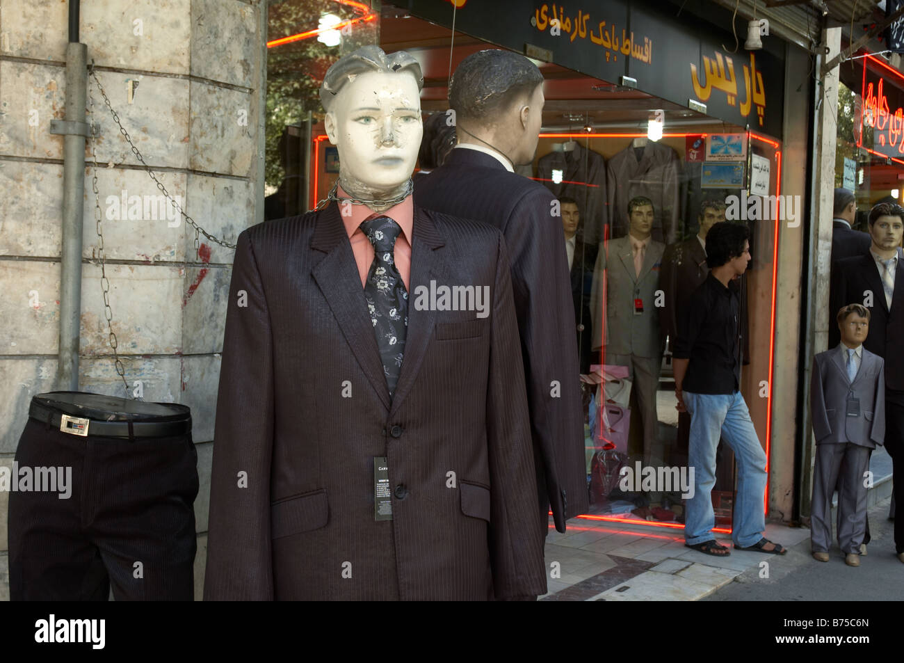 Il manichino indossa western indossare giacca e cravatta con un naso rotto e testa danneggiata, incatenato ad un tubo esterno di un negozio a Teheran. Foto Stock