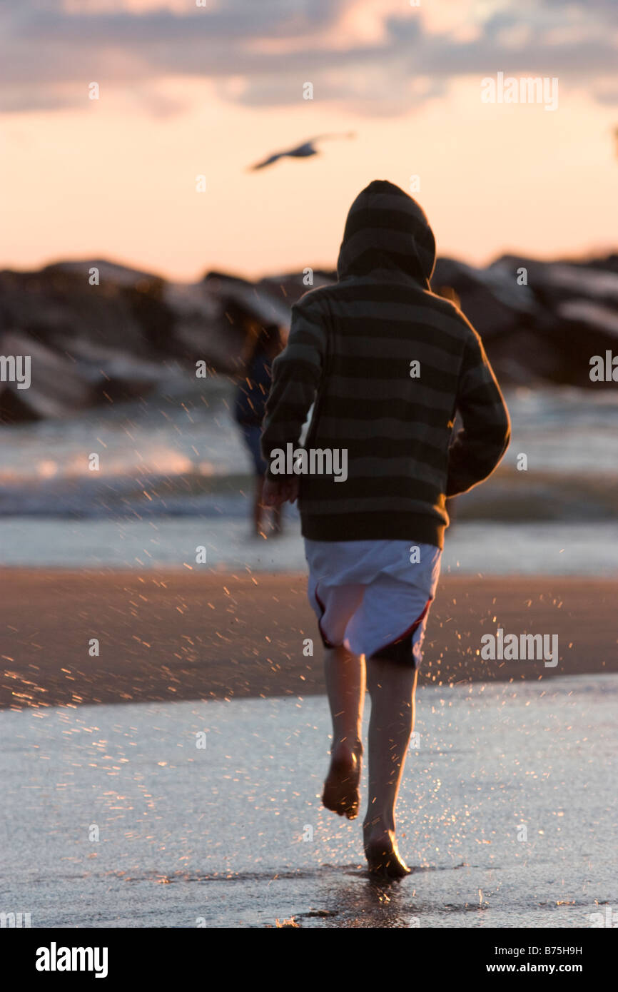 Ragazzo che corre verso l'acqua e le rocce in spiaggia Foto Stock