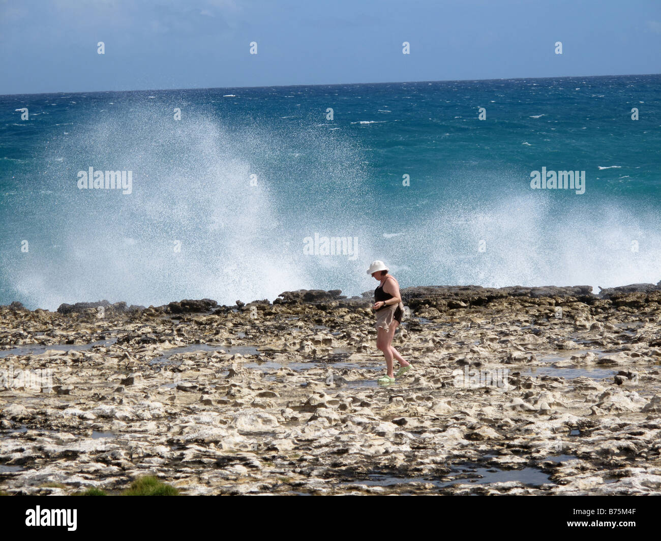 Una donna cammina passato Ponte Devils rock formazione come il mare riprese attraverso un foro di sfiato in Antigua nei Caraibi Foto Stock