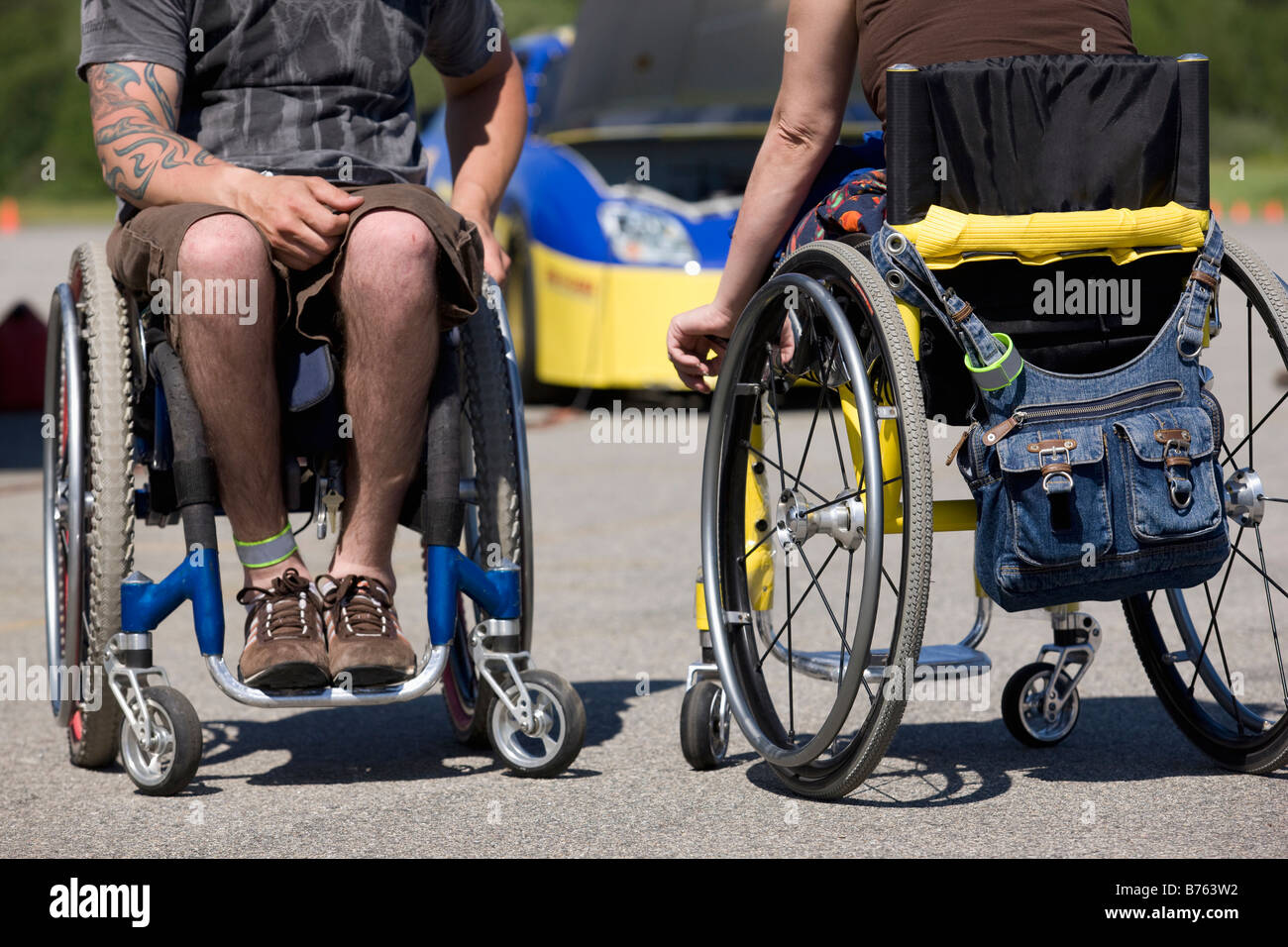 Due handicap auto racers su sedie a rotelle, bassa sezione, auto in background Foto Stock