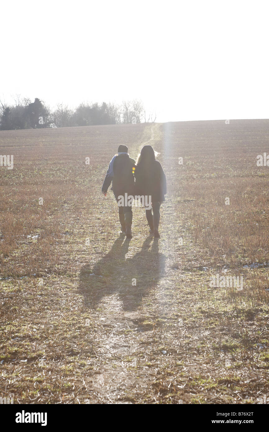 Lens Flare vista nel sole con la madre e la figlia sulla passeggiata invernale sul percorso in campo Foto Stock