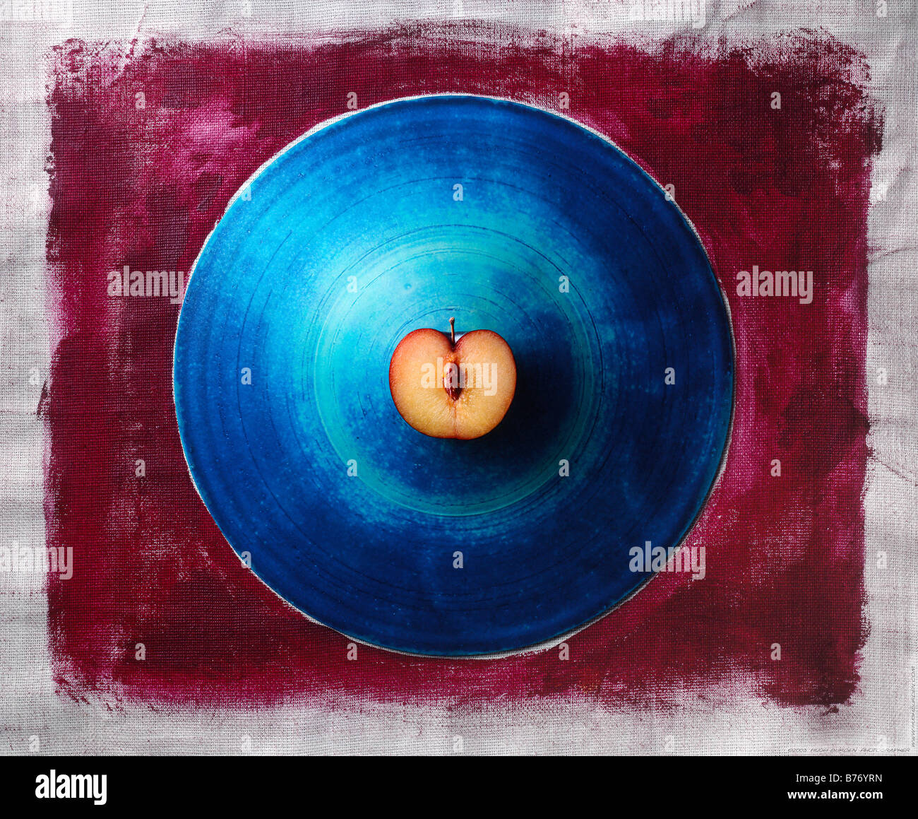 Prugna tagliata a metà seduta sulla piastra blu sulla tela dipinta sullo sfondo Foto Stock