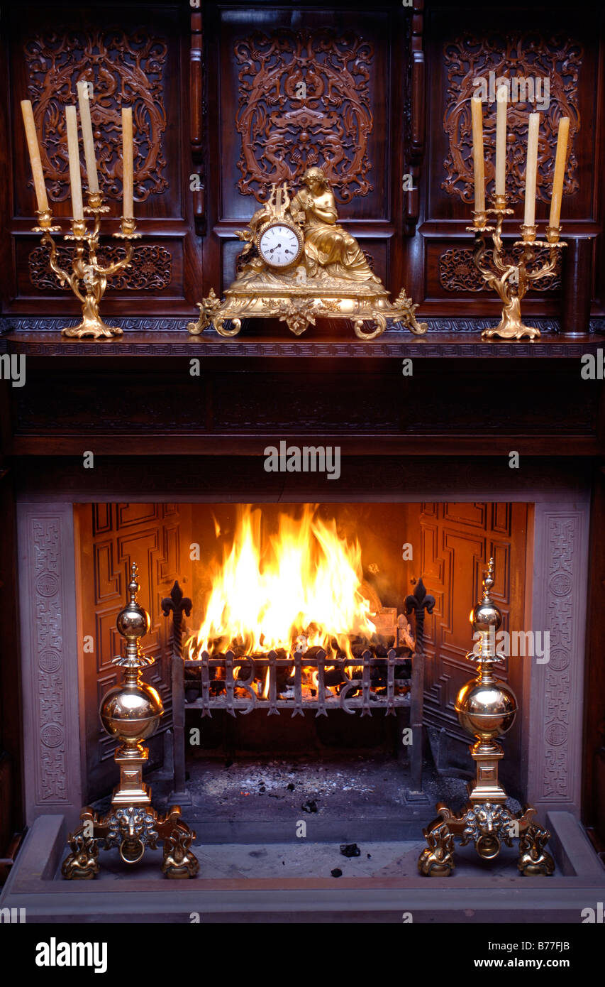 Un fuoco aperto in una casa di campagna con una orientale in legno scolpito e surround rococò francese orologio a mantello Foto Stock