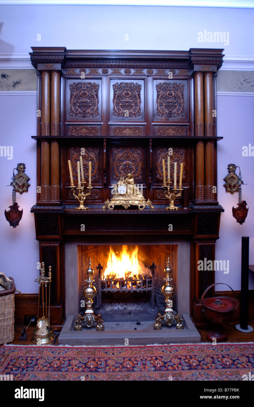 Un fuoco aperto in una casa di campagna con una orientale in legno scolpito e surround rococò francese orologio a mantello Foto Stock