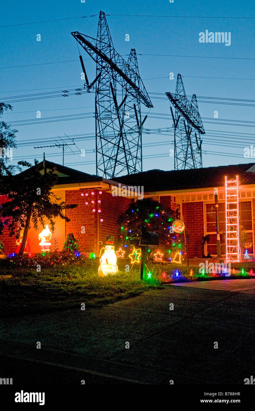Le luci di Natale festooning una casa suburbana in Australia contro uno sfondo di linee elettriche ad alta tensione Foto Stock