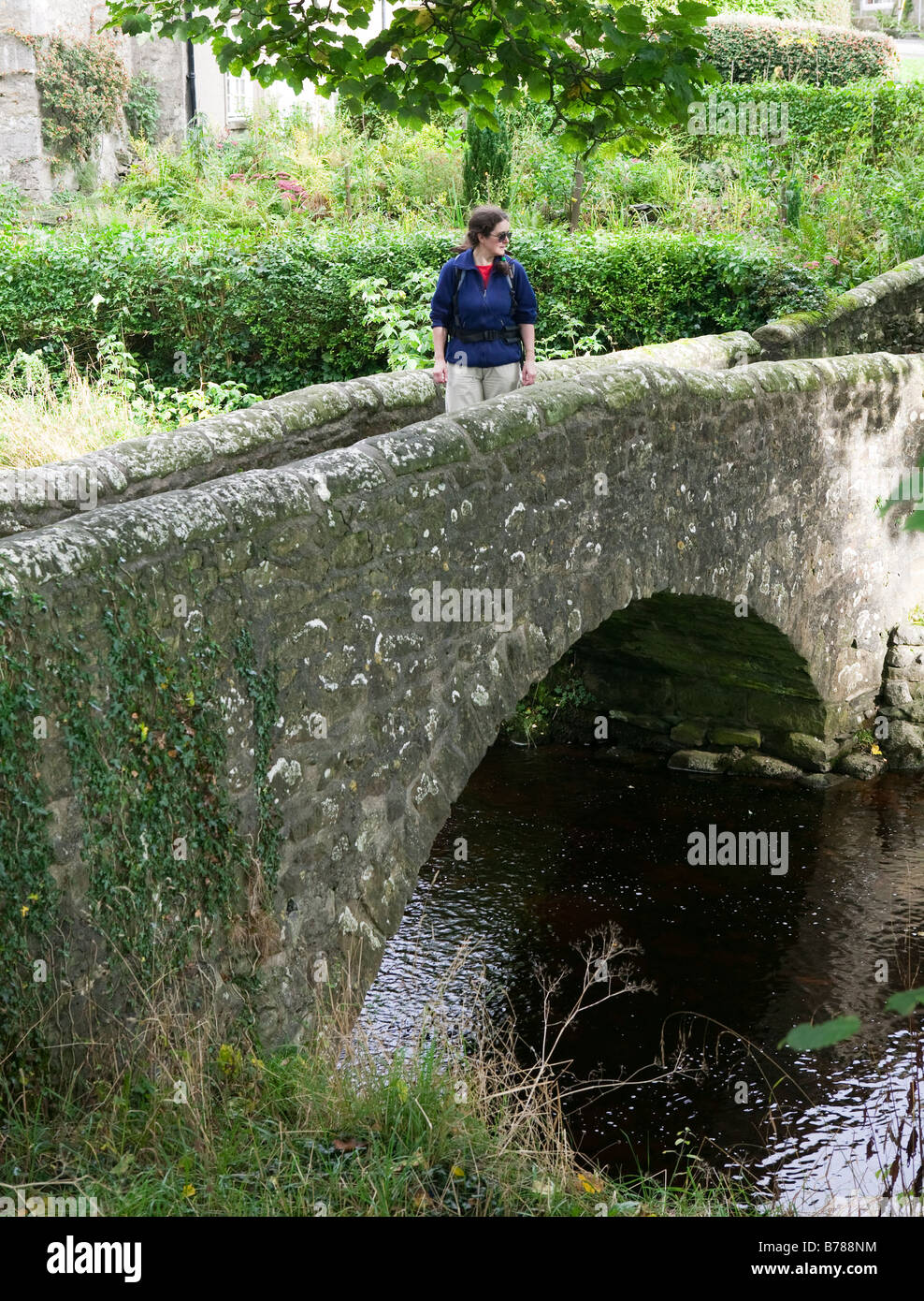 La donna a piedi attraverso un antico ponte in pietra nel villaggio di Clapham England Regno Unito Foto Stock La donna a piedi attraverso un antico ponte in pietra nel villaggio di Clapham England Regno Unito Foto Stock