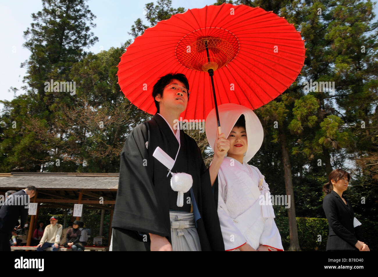 Matrimonio giapponese giovane indossando il tradizionale matrimonio kimono, sposa che indossa un cofano, sposo tenendo un ombrellone rosso nella parte anteriore del th Foto Stock