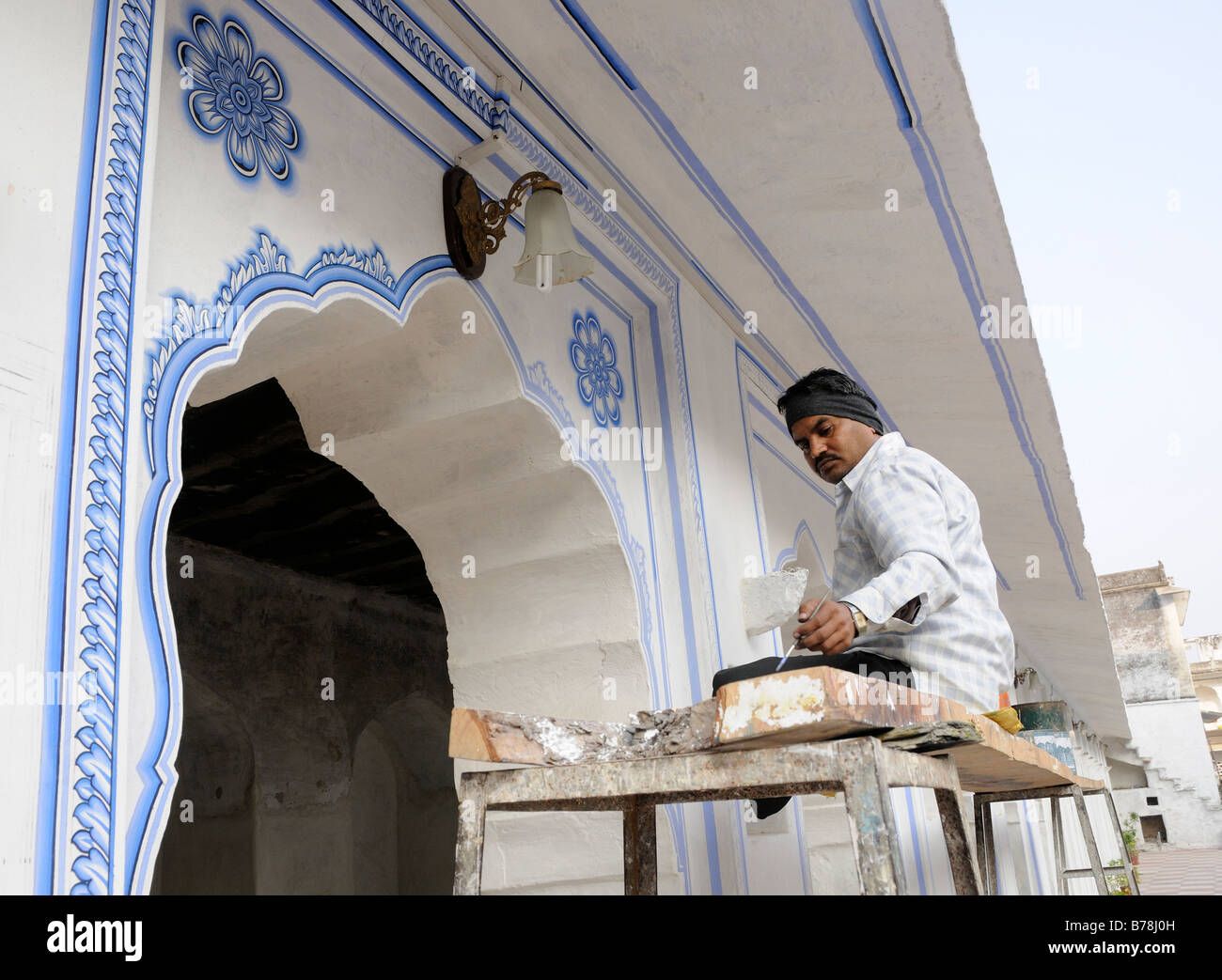 Un esperto pittore decora le pareti bianche di un colonnato con tradizionale blu modelli di ripetizione. Foto Stock