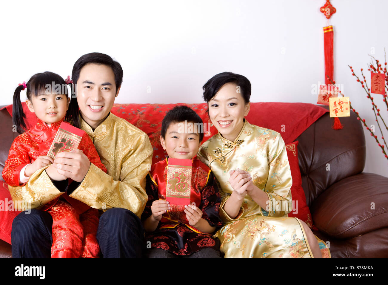 Giovane famiglia con due bambini in abiti tradizionali holding buste rosse e sorridente alla fotocamera Foto Stock