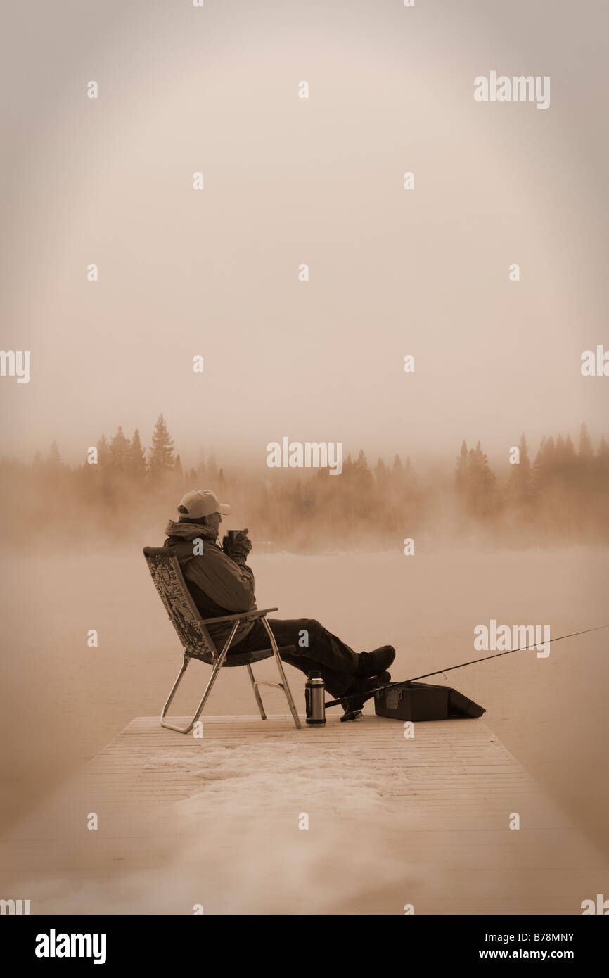 Un pescatore seduto su una dock in inverno con una tazza di caffè a Donner Lake in California Foto Stock