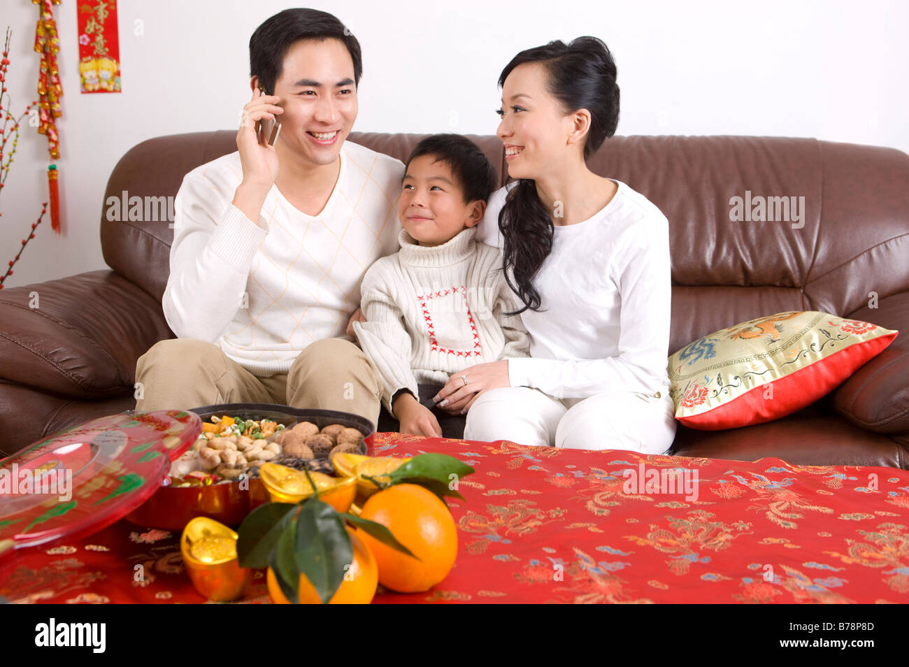 Coppia giovane con un bambino seduto sul divano e sorridente felicemente al telefono Foto Stock