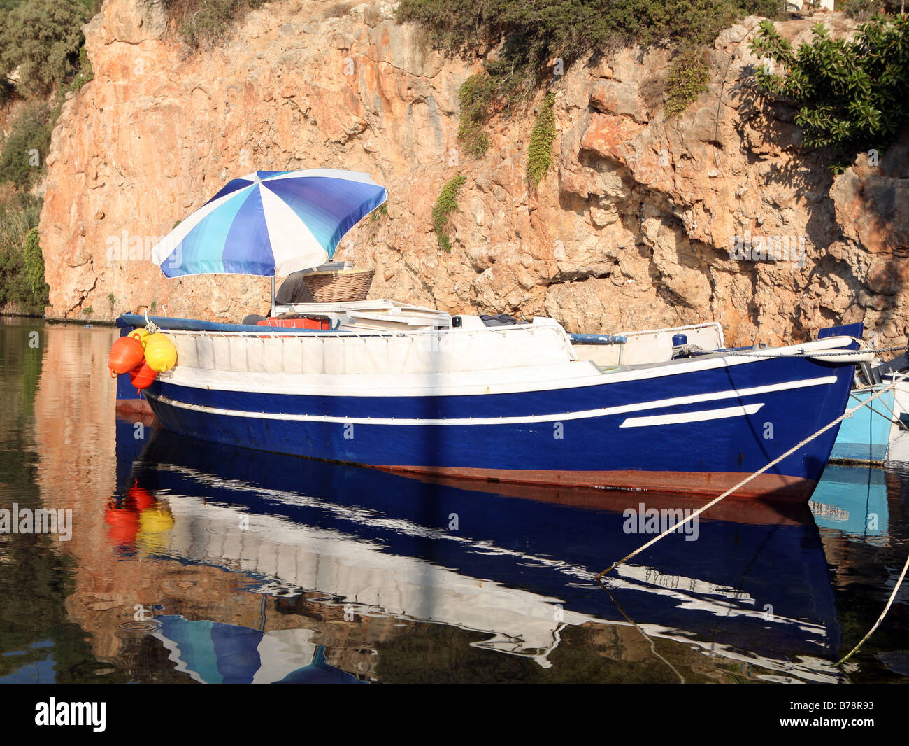 Una barca da pesca sul lago a Aghios Nikolaos, Creta, Grecia, nelle prime ore del mattino. L'ombrello è di proteggere il pescatore. Foto Stock