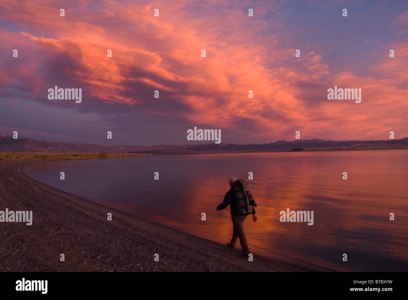 Un uomo che passeggia lungo la riva del lago Mono con acqua riflettente e nuvole in California Foto Stock