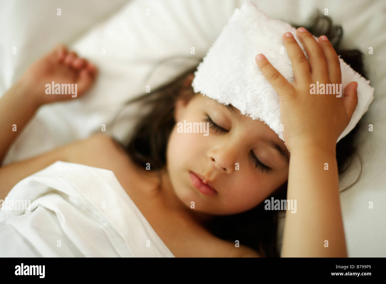 Bambina di cinque anni con flanella fresca sulla testa nel letto con lenzuola bianche Foto Stock
