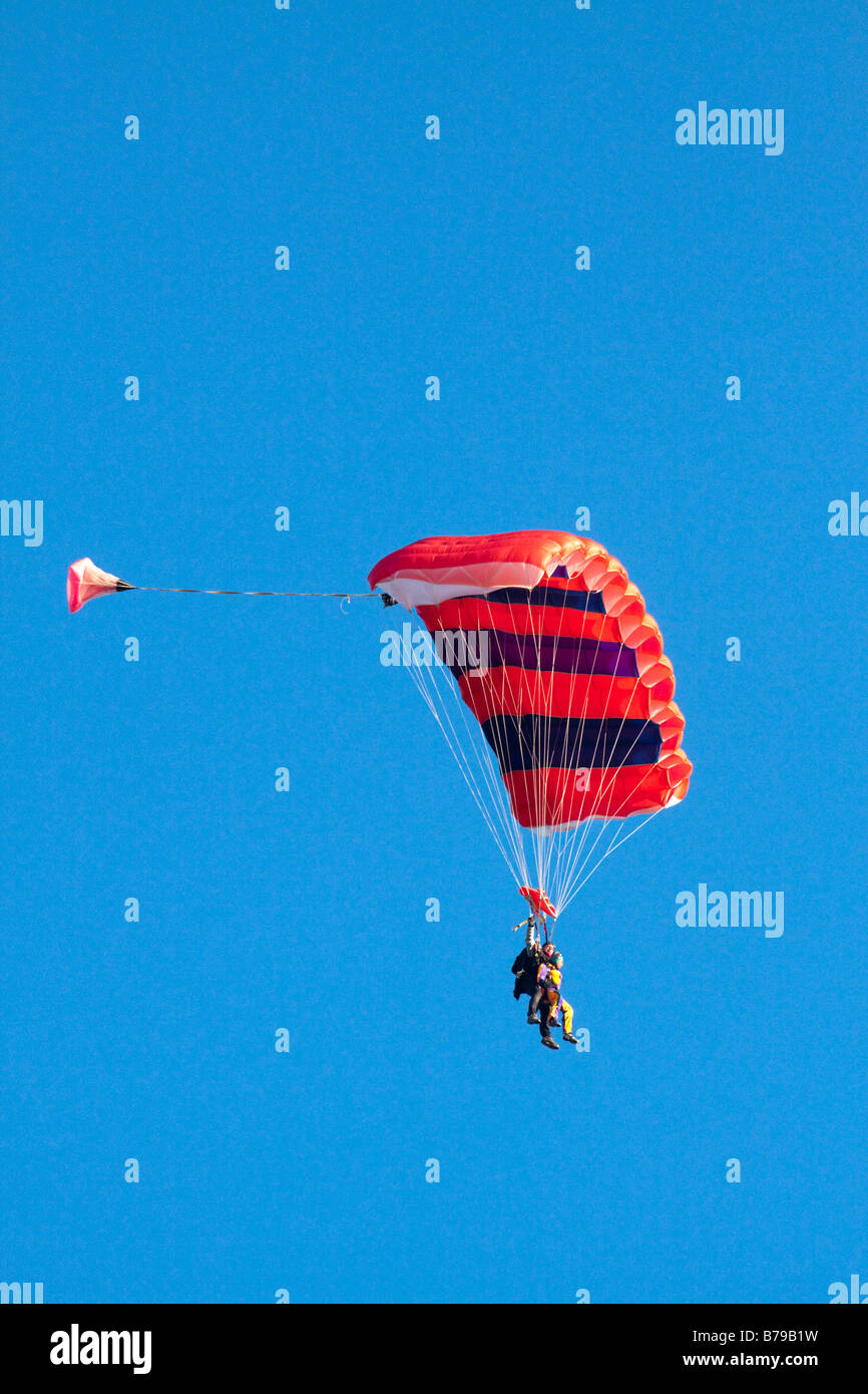 Paracadutismo TANDEM IN INGHILTERRA un rosso paracadute striato portante due persone scivola attraverso il cielo blu Foto Stock