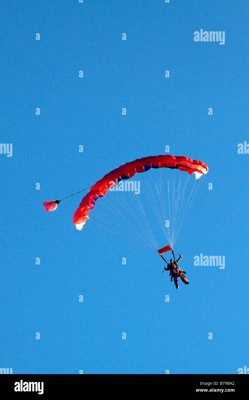 Paracadutismo TANDEM IN INGHILTERRA un rosso paracadute striato portante due persone scivola attraverso il cielo blu Foto Stock