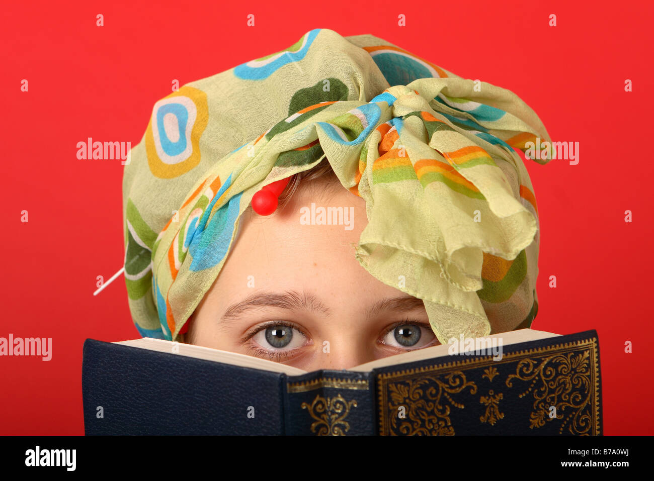 Ragazza adolescente indossando dei bigodini e la testa sciarpa cercando in vecchio stile la lettura di un libro Foto Stock