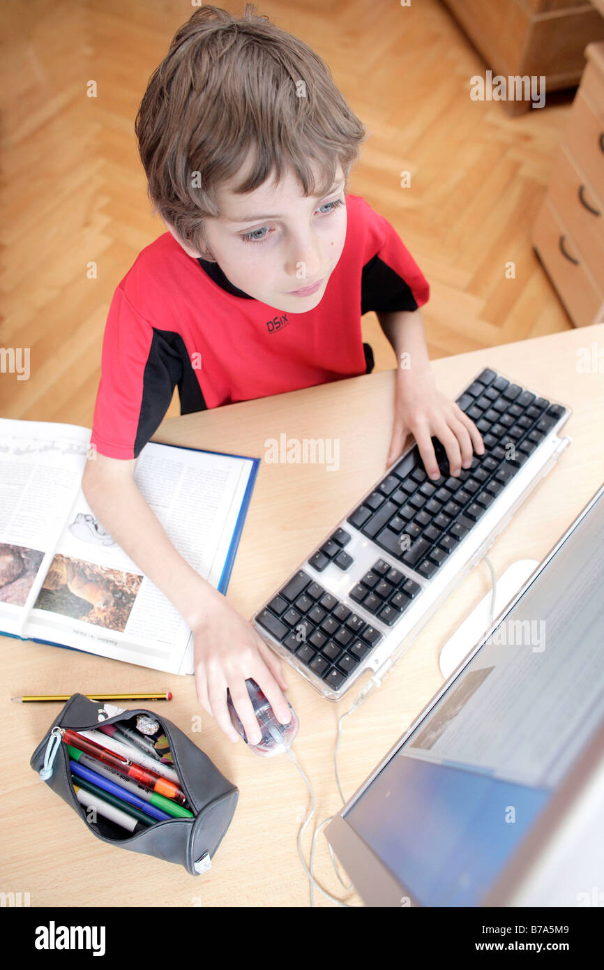Giovani 10 anno vecchio ragazzo al computer facendo i suoi compiti Foto Stock
