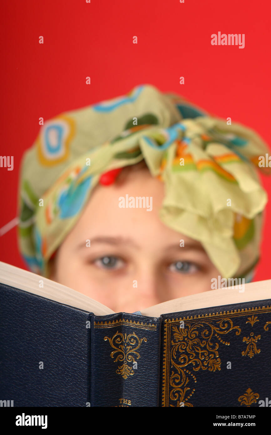 Un libro che viene letto da una ragazza adolescente indossando dei bigodini e la testa sciarpa cercando di vecchio stile Foto Stock