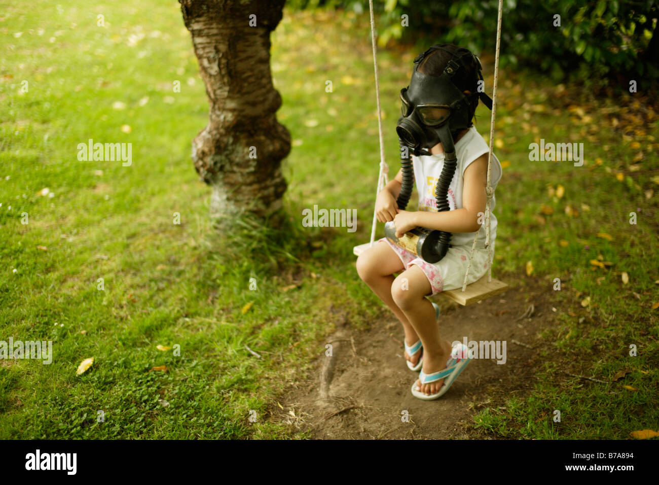 Bambina di cinque anni si siede su swing che indossa una maschera a gas Foto Stock