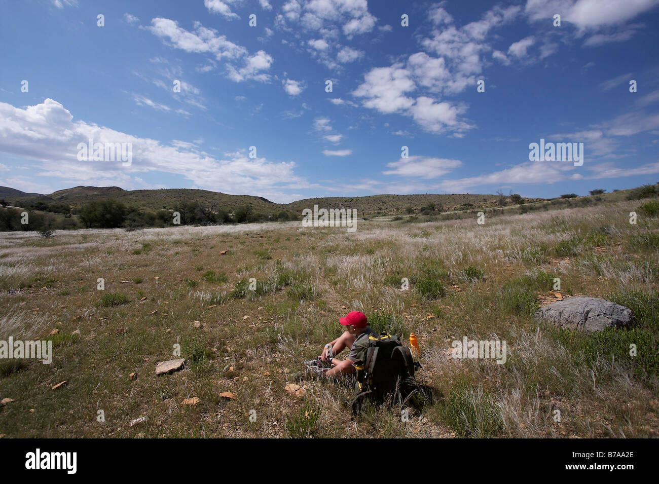 Un ragazzo adolescente in un cappuccio rosso seduto a riposare durante il Naukluft sentiero escursionistico Foto Stock