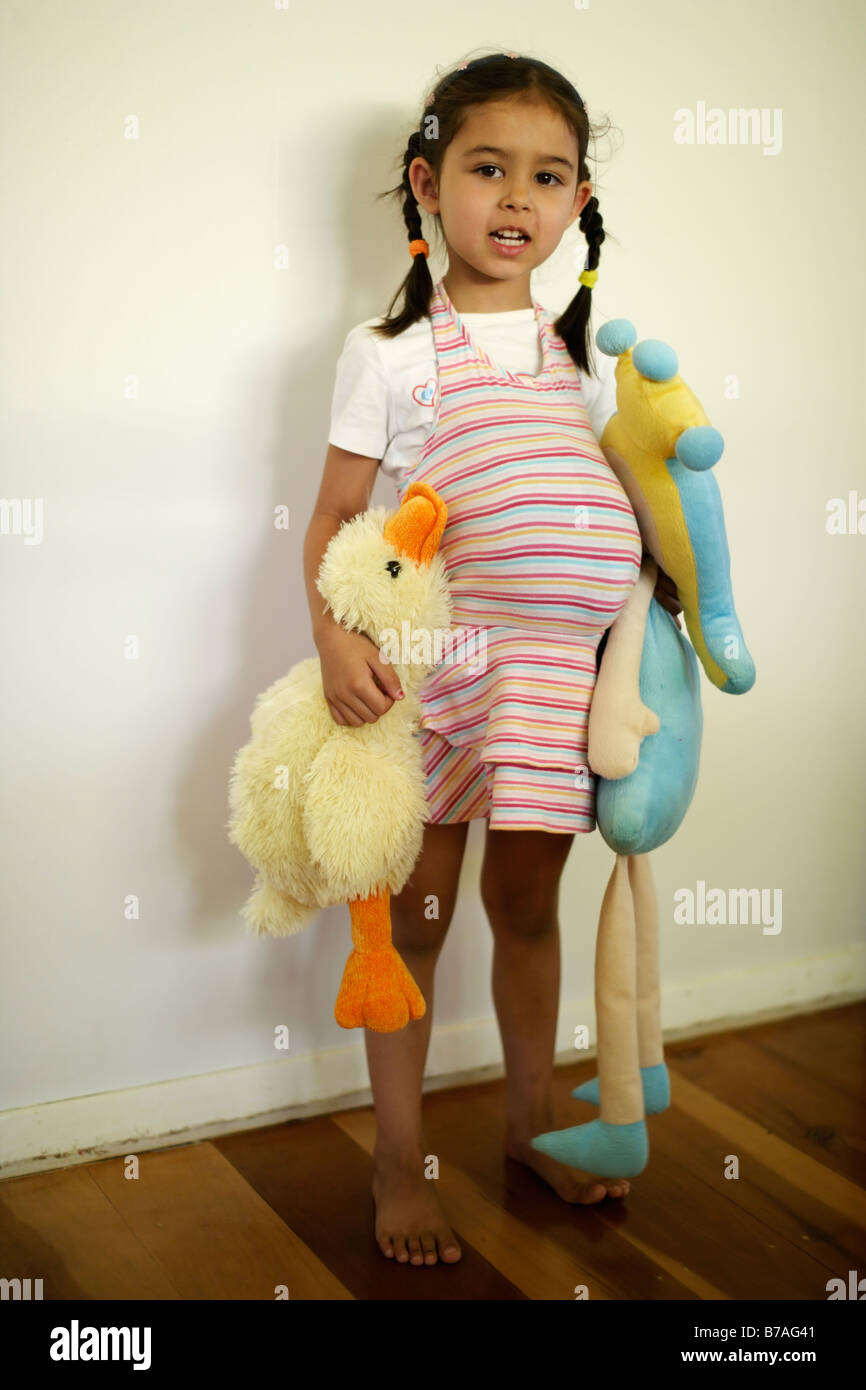 Bambina di cinque anni finge di essere grassi o incinta da ripieno un giocattolo morbido sotto il suo vestito Foto Stock