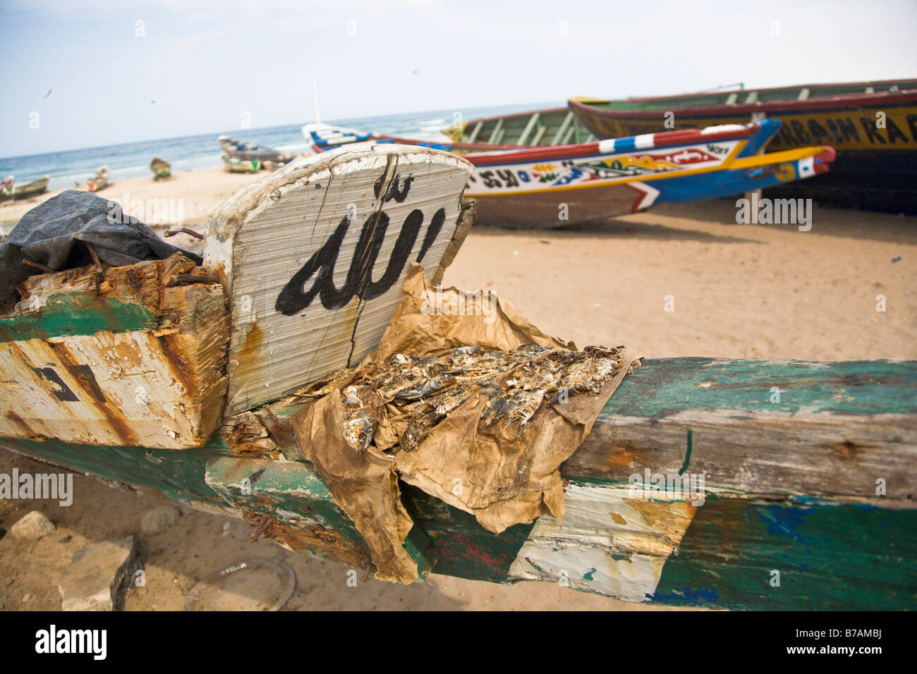 Un lotto di pesce è prevista ad asciugare su uno dei colori vivaci dipinte di barche da pesca che la linea della spiaggia di Yoff, Senegal Foto Stock