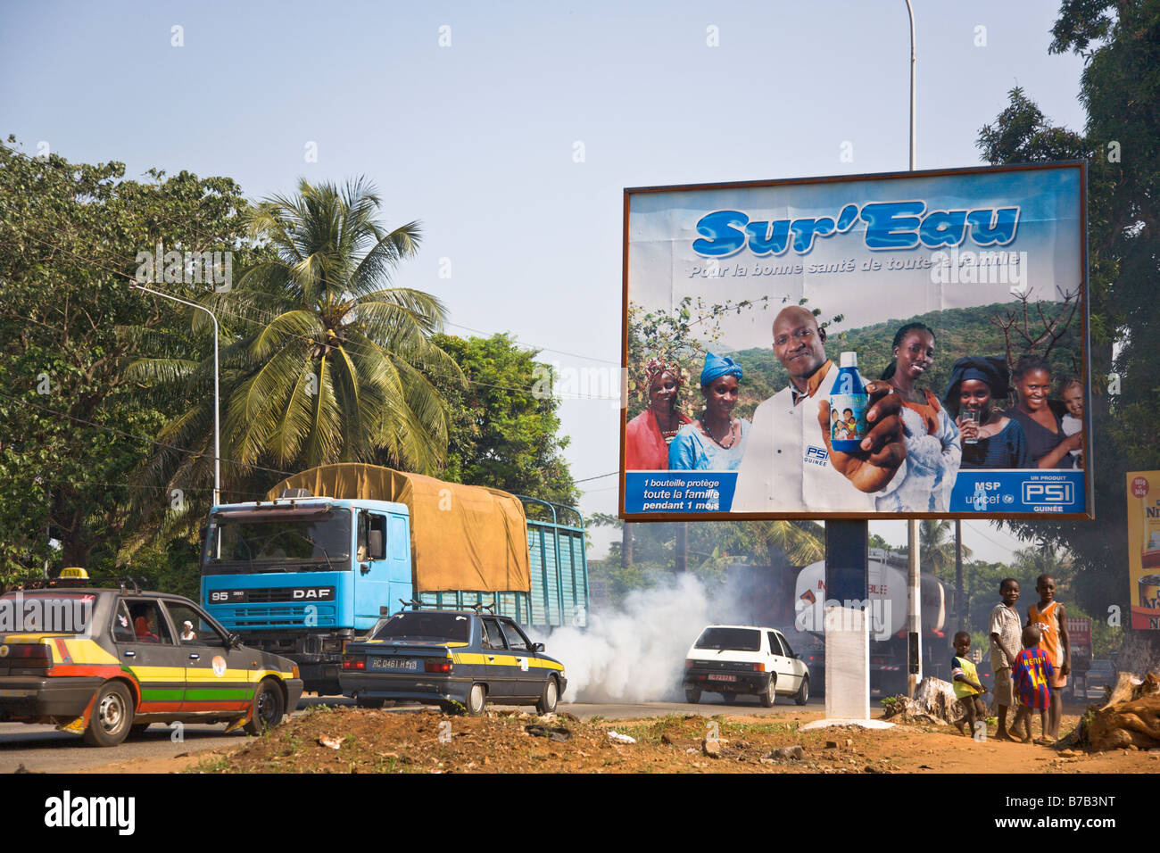 Bambini sostare al di sotto di una pubblicità tramite Affissioni Sur Eau su una strada trafficata attraverso la Guinea la capitale Conakry. Foto Stock