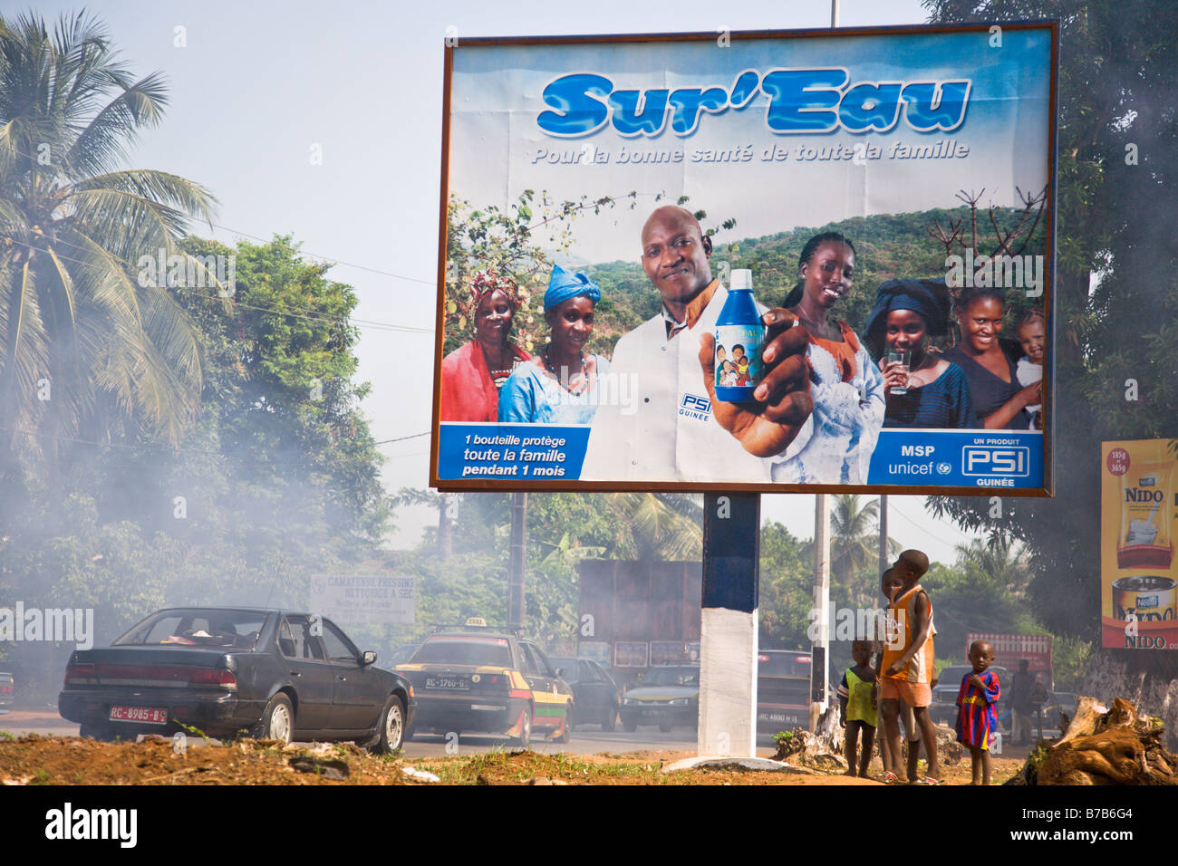 I bambini guardano fino a una pubblicità tramite Affissioni Sur Eau su una strada trafficata attraverso la Guinea la capitale Conakry. Foto Stock